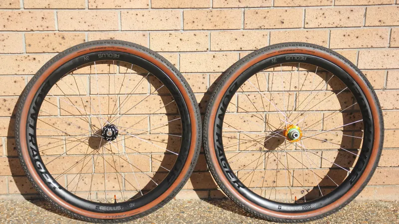 A pair of finished gravel wheels with tan-wall tyres, standing against a brick wall