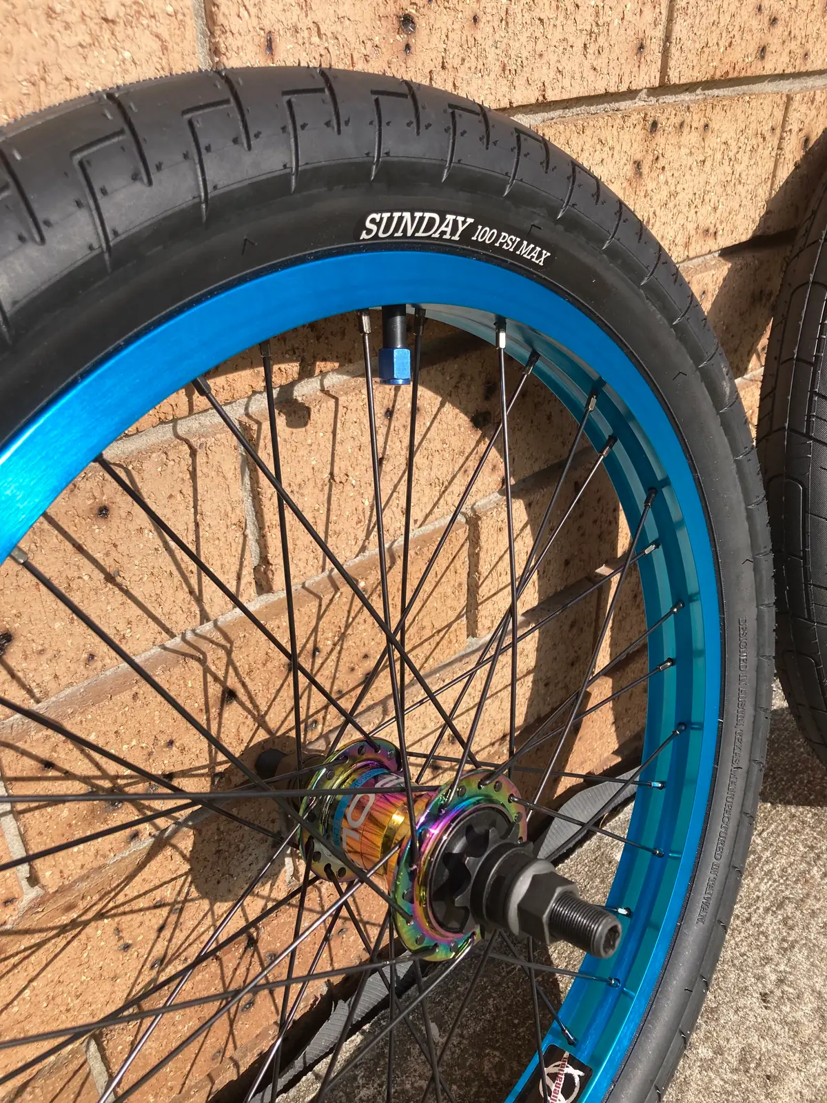 Close-up of an oil-slick hub laced into the blue rim, with a Sunday tyre fitted