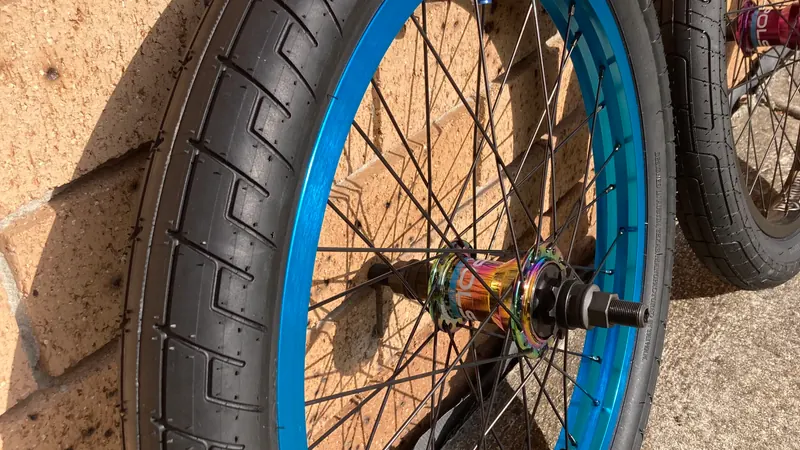A finished 20-inch BMX rear wheel with a blue rim, propped against a brick wall