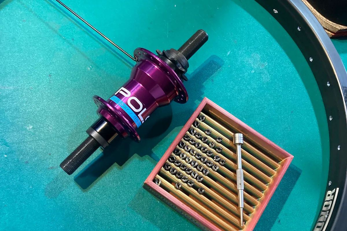 A custom hub laid out beside a tray of brass nipples and cut spokes, ready to lace